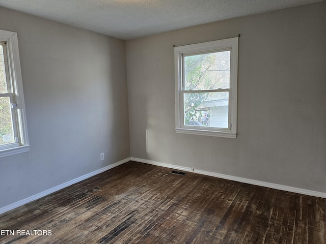 empty room featuring a textured ceiling, dark wood-style flooring, visible vents, and baseboards