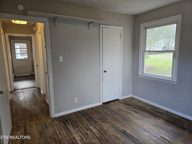 unfurnished bedroom with a textured ceiling, baseboards, dark wood-type flooring, and multiple windows