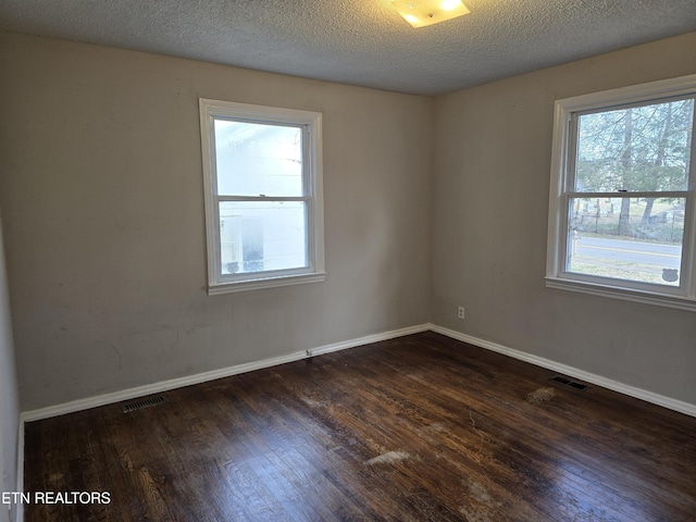 empty room featuring dark wood-style flooring, visible vents, and baseboards