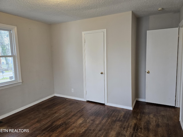 unfurnished bedroom with multiple windows, dark wood finished floors, and baseboards