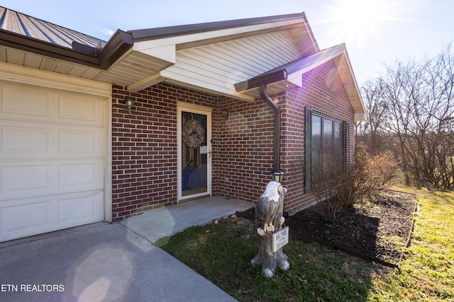 view of exterior entry with a standing seam roof, brick siding, a garage, and metal roof