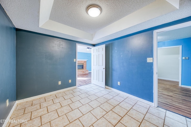 spare room featuring light tile patterned floors, ceiling fan, a textured ceiling, baseboards, and a brick fireplace