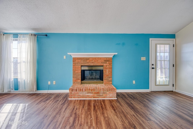 unfurnished living room with a fireplace, a textured ceiling, baseboards, and wood finished floors