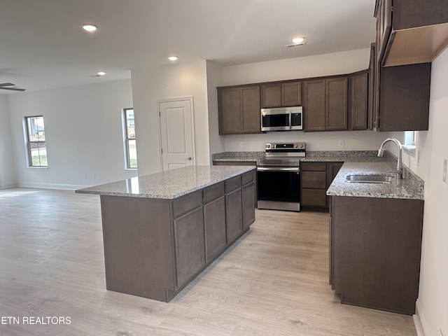 kitchen with sink, light hardwood / wood-style flooring, appliances with stainless steel finishes, a kitchen island, and light stone countertops