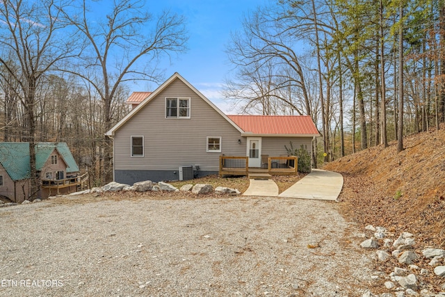 rear view of property with metal roof, a wooden deck, and driveway