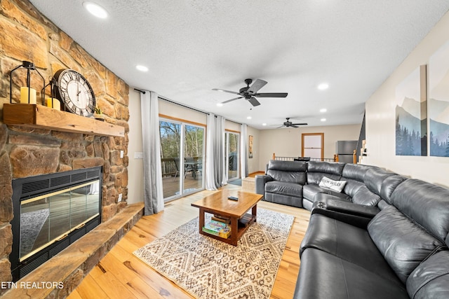 living room with a textured ceiling, a stone fireplace, wood finished floors, and recessed lighting