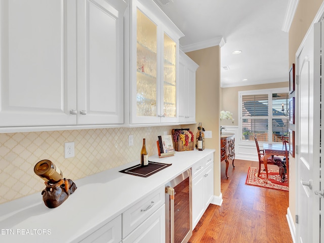 kitchen featuring light wood finished floors, light countertops, wine cooler, white cabinets, and crown molding