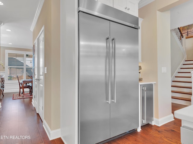 kitchen with built in fridge, wine cooler, white cabinets, crown molding, and dark wood-style flooring