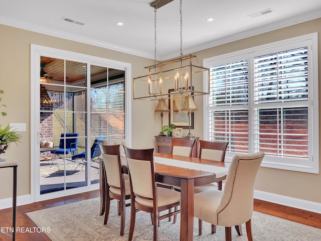 dining area with visible vents, wood finished floors, a chandelier, and ornamental molding