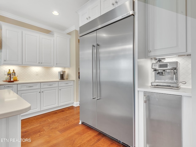 kitchen with light wood-type flooring, light countertops, stainless steel built in fridge, ornamental molding, and white cabinetry