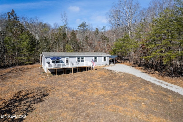 manufactured / mobile home featuring dirt driveway, a wooded view, and a wooden deck