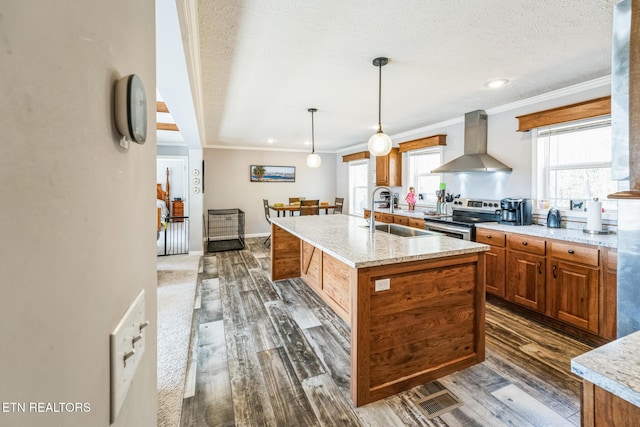 kitchen with a sink, wall chimney range hood, stainless steel electric stove, an island with sink, and pendant lighting