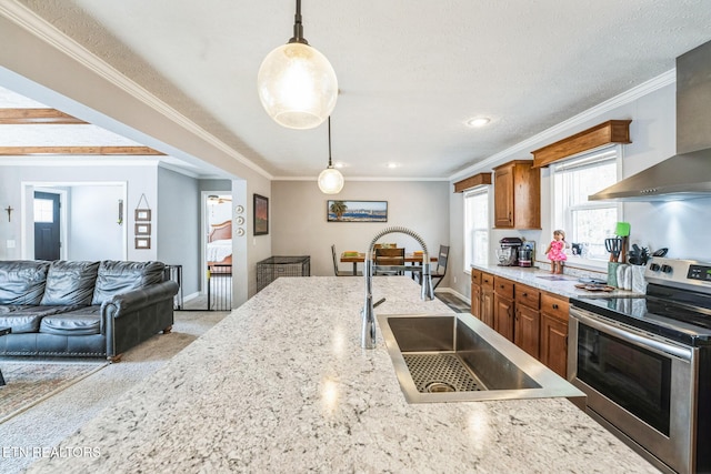 kitchen with pendant lighting, brown cabinets, stainless steel electric stove, a sink, and wall chimney exhaust hood