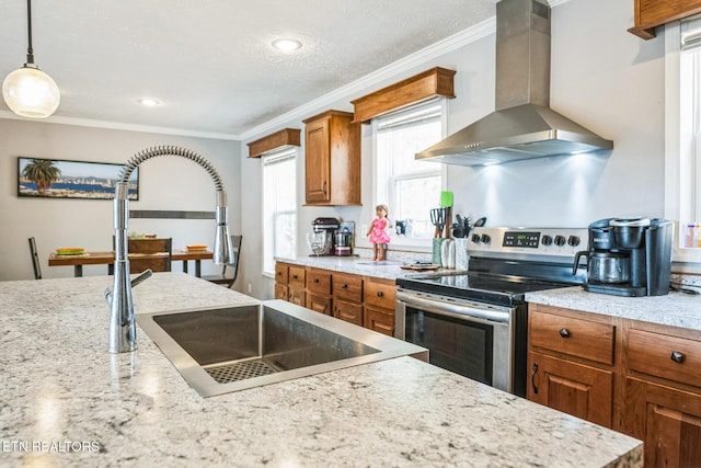 kitchen with brown cabinets, stainless steel electric stove, light countertops, wall chimney range hood, and pendant lighting