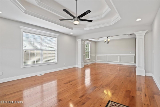 unfurnished living room with light wood-type flooring, ornate columns, a raised ceiling, and crown molding