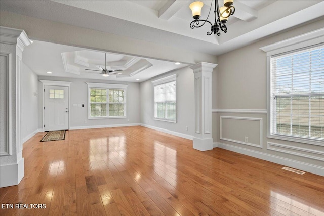 unfurnished living room featuring a tray ceiling, visible vents, light wood-style flooring, and ornate columns