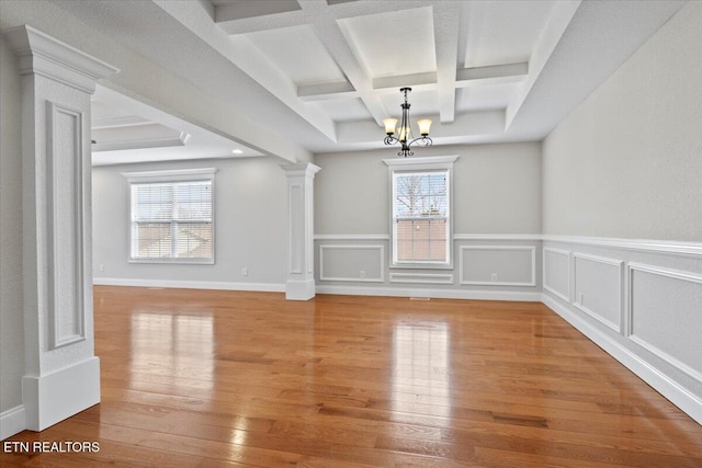 unfurnished dining area featuring an inviting chandelier, decorative columns, light wood finished floors, and a wealth of natural light