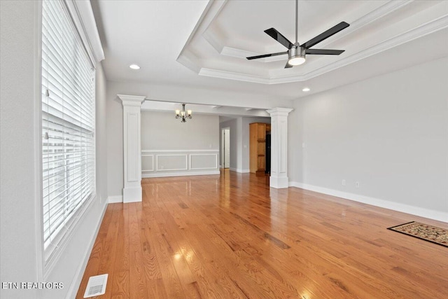 unfurnished living room with visible vents, a raised ceiling, light wood-type flooring, ornate columns, and ceiling fan with notable chandelier