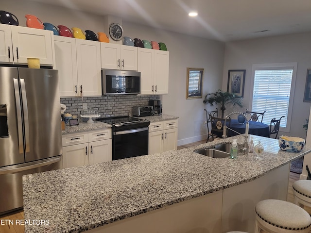 kitchen with white cabinets, decorative backsplash, light stone counters, stainless steel appliances, and a sink