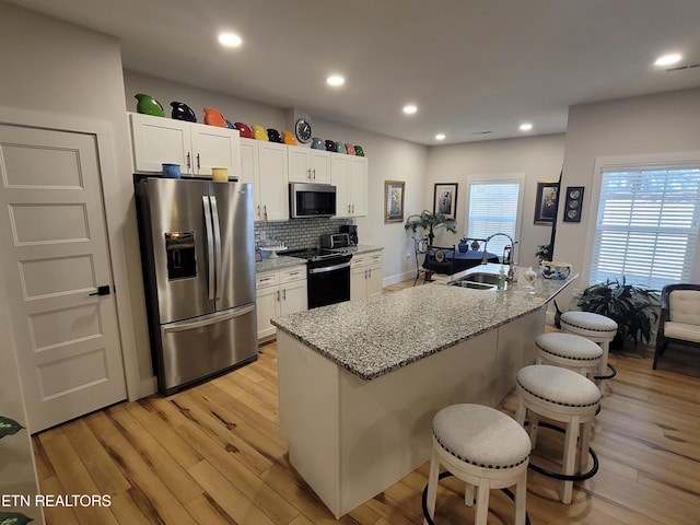 kitchen featuring stainless steel appliances, a breakfast bar, a sink, white cabinetry, and light wood finished floors