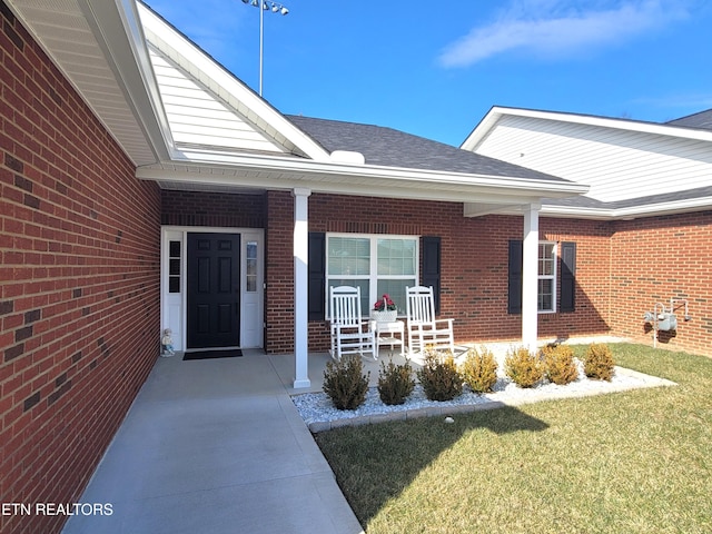 entrance to property featuring a shingled roof, a porch, and brick siding