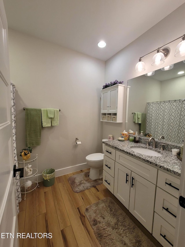 bathroom featuring baseboards, a shower with shower curtain, toilet, wood finished floors, and vanity