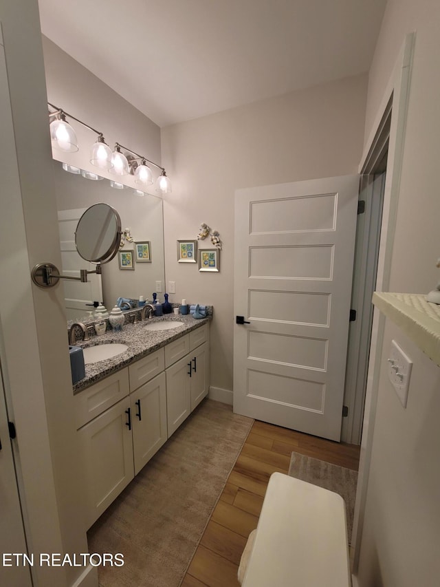 full bathroom with double vanity, baseboards, a sink, and wood finished floors