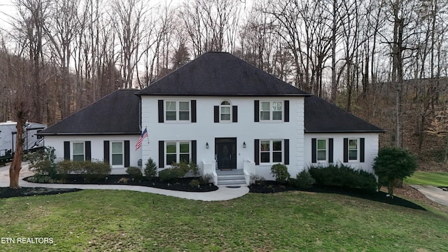 colonial house featuring a shingled roof and a front yard