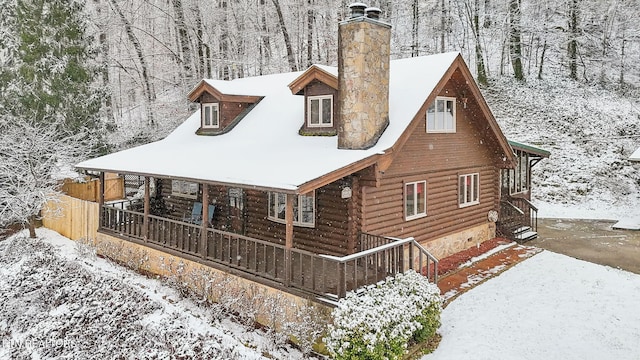 view of front of house with covered porch, log exterior, and a chimney