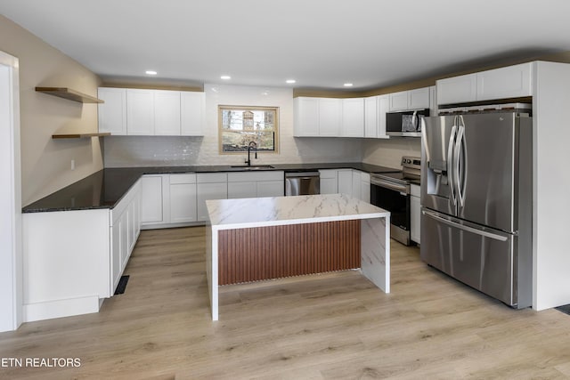 kitchen featuring light wood-type flooring, stainless steel appliances, white cabinets, a center island, and sink