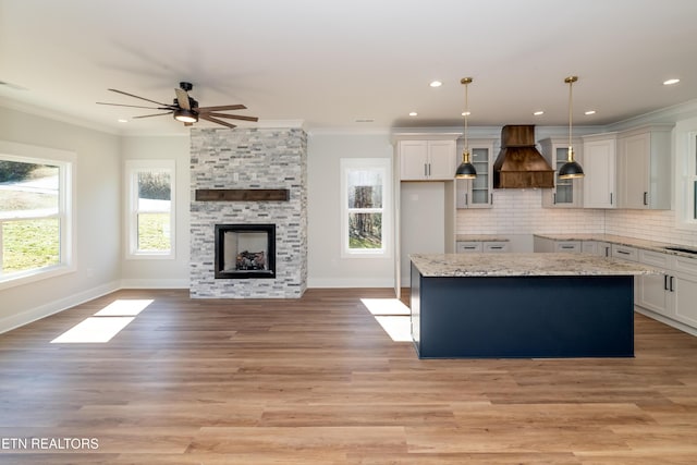 kitchen featuring hanging light fixtures, a center island, light stone countertops, custom exhaust hood, and decorative backsplash