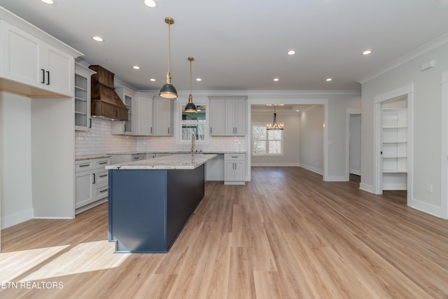 kitchen with custom exhaust hood, pendant lighting, a kitchen island, crown molding, and light stone countertops