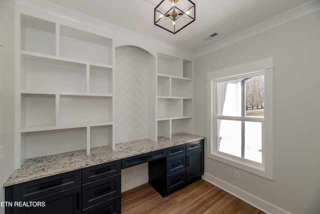 unfurnished office with crown molding, built in desk, a notable chandelier, and wood-type flooring