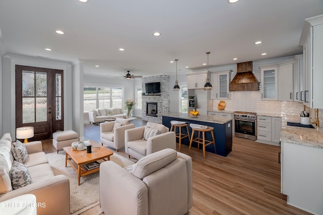 living room featuring light hardwood / wood-style flooring, a stone fireplace, sink, ornamental molding, and ceiling fan