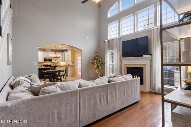 living room featuring a warm lit fireplace, visible vents, arched walkways, wood finished floors, and ceiling fan with notable chandelier