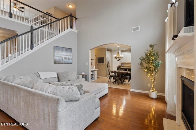 living area featuring wood finished floors, visible vents, a fireplace with flush hearth, arched walkways, and a high ceiling