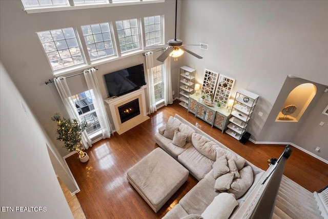 living area with a towering ceiling, a wealth of natural light, a fireplace with flush hearth, and wood finished floors