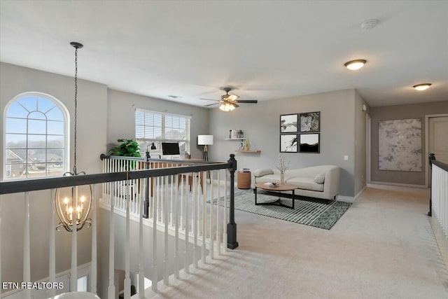 living area featuring baseboards, ceiling fan with notable chandelier, and light colored carpet