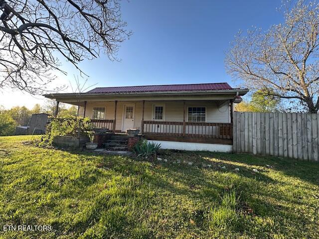 view of front of house with fence, a front yard, metal roof, and covered porch
