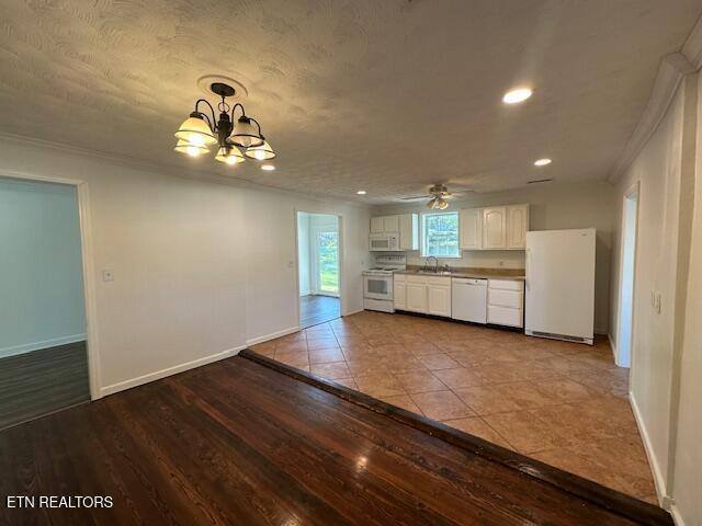 kitchen with ornamental molding, a sink, white appliances, baseboards, and white cabinetry