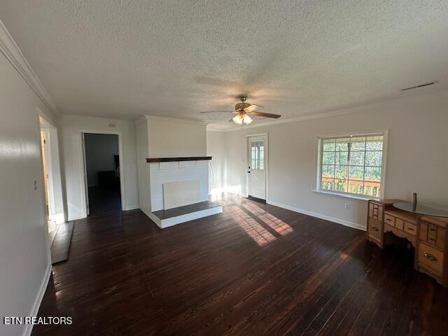 unfurnished living room featuring a textured ceiling, a ceiling fan, ornamental molding, a brick fireplace, and dark wood-style flooring