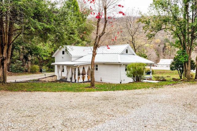 view of front facade with gravel driveway, covered porch, and metal roof