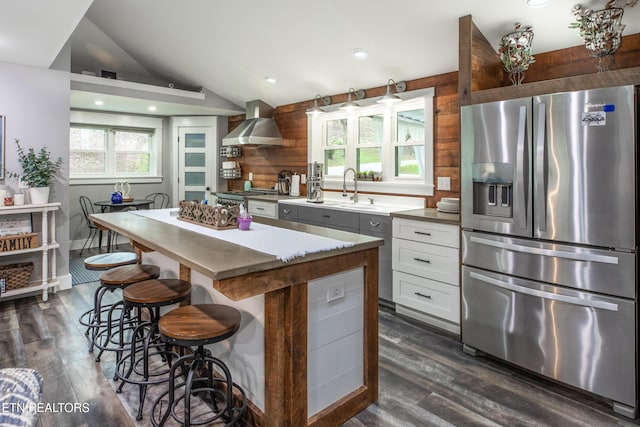 kitchen with white cabinets, vaulted ceiling, a kitchen island, wall chimney range hood, and stainless steel fridge