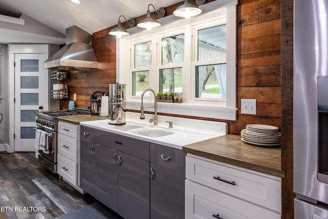 kitchen featuring range hood, dark countertops, appliances with stainless steel finishes, white cabinets, and a sink