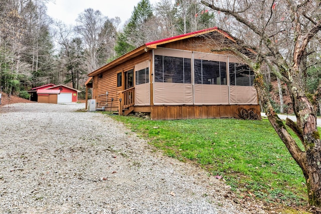 view of front facade featuring a sunroom, a front yard, a detached garage, and an outbuilding