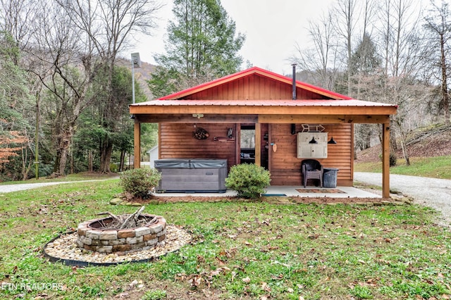 exterior space featuring an outdoor fire pit, metal roof, a hot tub, and a front lawn