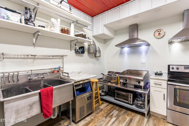 kitchen with white cabinets, stainless steel electric range oven, wall chimney range hood, and wood finished floors