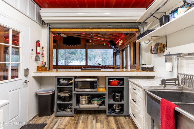 kitchen with white cabinets, stainless steel microwave, wood finished floors, light countertops, and open shelves