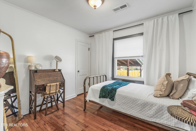 bedroom with baseboards, visible vents, wood finished floors, and ornamental molding