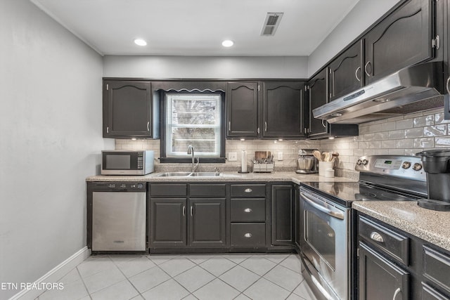kitchen with light tile patterned floors, under cabinet range hood, stainless steel appliances, a sink, and tasteful backsplash